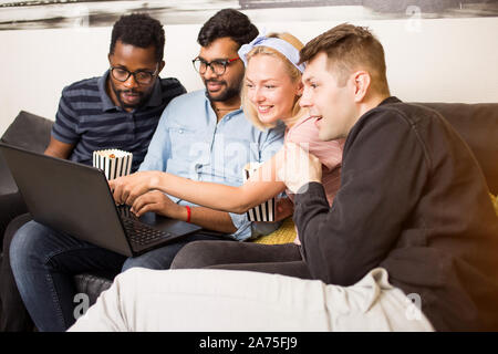 Positive young multi ethnic students watching video on laptop computer while collaborating on project, preparing for exams together. Friends having fu Stock Photo