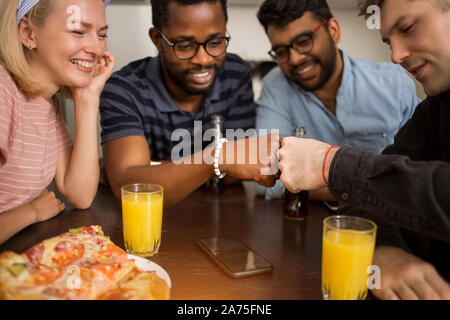Group of four students having fun in kitchen. Young african and caucasian men giving fist bump, smiling celebrating success with friends. Friendship, Stock Photo