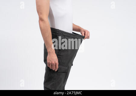 Thin man stretching his pants to show loss of weight after diet. Person isolated on white background with copy space. Different size clothes delivery. Stock Photo