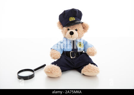 Police officer teddy bear in uniform and a magnifying glass isolated against white background Stock Photo