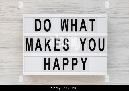 'Do what makes you happy' words on a lightbox on a white wooden surface, top view. Overhead, from above, flat lay. Stock Photo