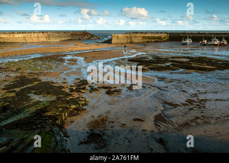 Staithes Harbour North Yorkshire at low tide showing the sandy and rocky bottom and a line of fishing boats lie on the sand Stock Photo