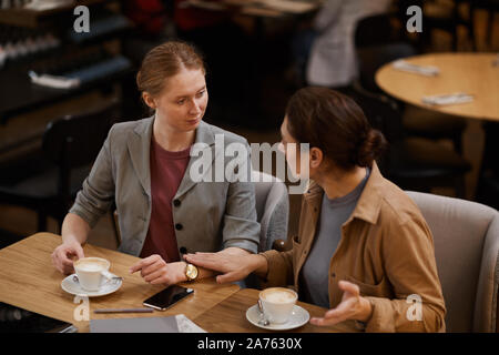 Two young businesswomen drinking coffee and discussing working moments during coffee break in cafe Stock Photo