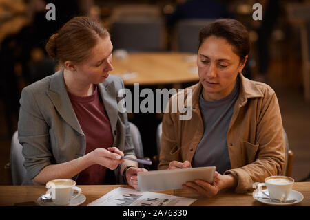 Two business partners using digital tablet and discussing online work together at the table while drinking coffee in cafe Stock Photo