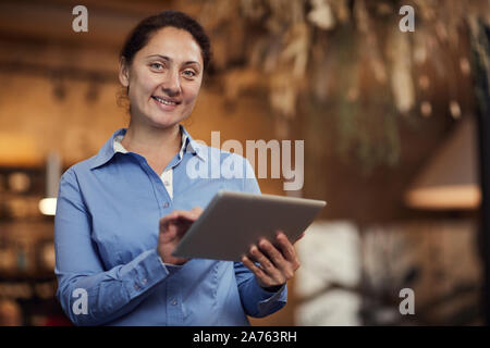 Portrait of mature businesswoman standing and smiling at camera while using digital tablet Stock Photo