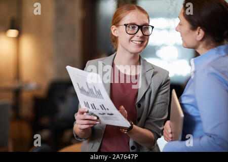 Young businesswoman in eyeglasses smiling and explaining to her partner financial report in her hands Stock Photo