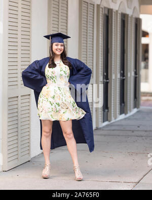 Graduating senior in cap and gown and floral dress poses on street Stock Photo