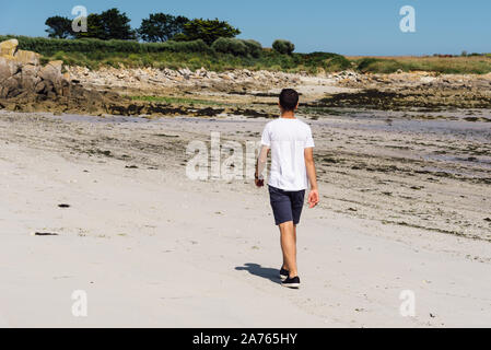 Full length portrait of an attractive young man walking along the seashore, he wears casual clothes. Stock Photo