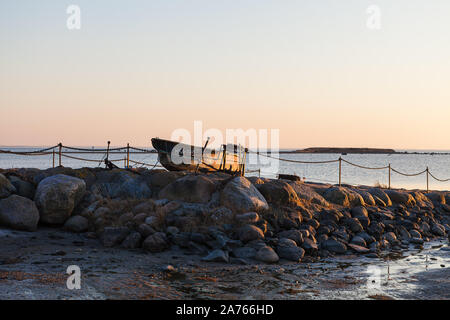 Old wooden fishing boat laying on the rocky shore of the sea at sunset Stock Photo