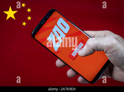Male hand holding smartfone with ZAO app logo and download button against China flag. Stock Photo