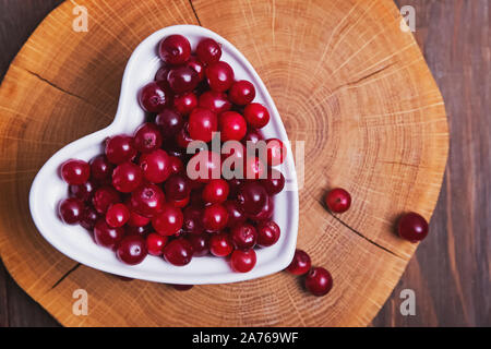 Fresh cranberry berries in heart shaped bowl on wooden board, top view Stock Photo