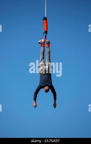 A man jumps with a bungee from a crane top against the blue sky. Unrecognizable person. Stock Photo