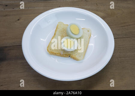 Half cutted hard boiled egg on toasted sandwich bread, ready to eat, in white plate, wooden table background Stock Photo
