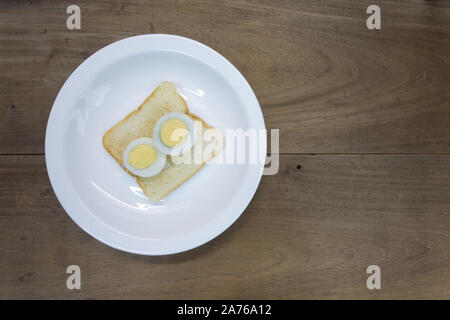 Half cutted hard boiled egg on toasted sandwich bread, ready to eat, in white plate, wooden table background Stock Photo