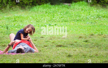 Caravaca, Spain, September 12, 2019: Family spend leisure time in picnic on sunny day at natural park. Father and daughter at the park lying on grass. Stock Photo