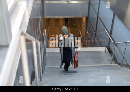 Woman wearing headscarf walking up stairs with briefcase Stock Photo