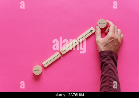 Male hand placing wooden pegs and circles to form a diagram with arrow pointing from word Start to Goal in a conceptual image of personal aspirations. Stock Photo