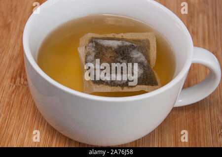 Cup of green tea with teabag, large white mug of this hot drink closeup on a wood table. Stock Photo
