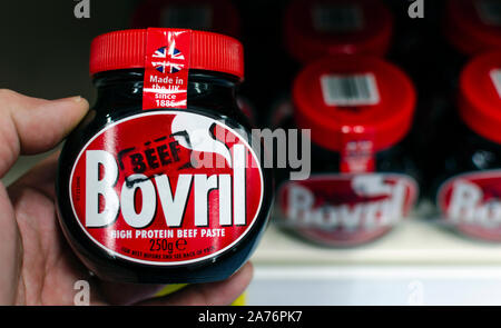 Bovril jar hold in a hand next to other jars on the shelf. Bovril is a thick and salty meat extract. Original British beef hot drink. Stock Photo