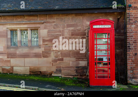 Iconic Red telephone box next to a very old stone wall seen in Oulton, Staffordshire, United kingdom. Stock Photo