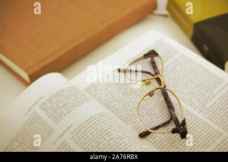 Scene where several books are seen, one of them opened by one of its pages, on which there are brown-framed glasses Stock Photo