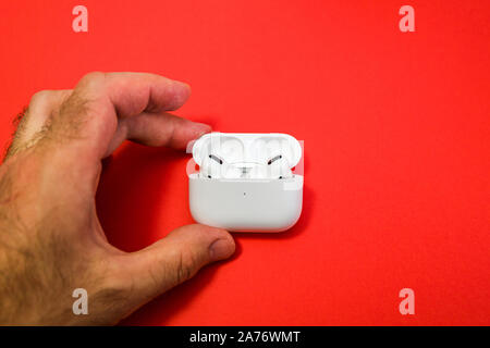 Paris, France - Oct 30, 2019: Man hand holding against red background New Apple Computers AirPods Pro headphones with Active Noise Cancellation for immersive sound Stock Photo