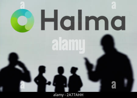 The Halma plc logo is seen on an LED screen in the background while a silhouetted person uses a smartphone (Editorial use only) Stock Photo