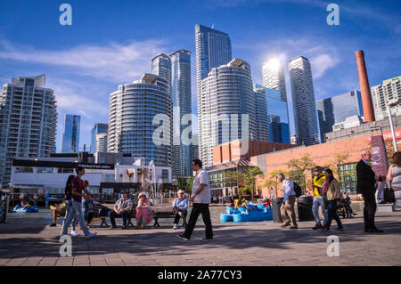 Toronto, Ontario, Canada - 2019 06 09: Torontonians and tourists walking along the promenade in the Harbourfront Toronto in front of high rise Stock Photo