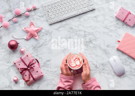 Christmas flat lay on marble table. Hands warming up from warm cup of cafe latte or hot chocolate with heart shape. Winter decorations: fir twigs, sof Stock Photo