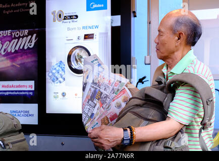 Singapore-17 MAR 2018:An old Chinese man reading newspaper at bus station Stock Photo
