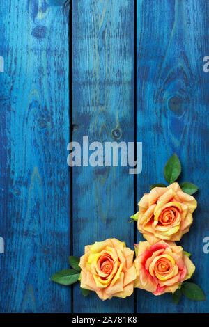 Romantic background with three orange rose flowers on blue wooden background Stock Photo