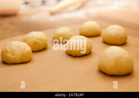 Raw homemade buns on kitchen table cooking for autumn holiday dining. Cozy home mood. Side view, copy space Stock Photo