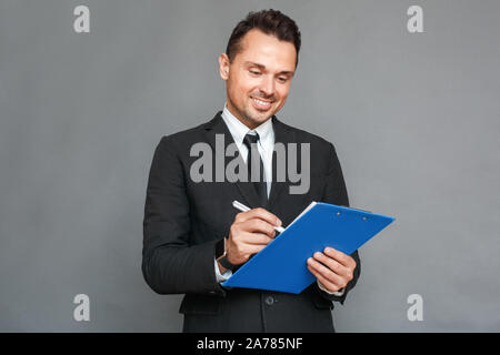 Businessman studio standing isolated on grey with clipboard taking notes smiling joyful Stock Photo