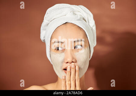 Beautiful woman with clay facial mask over orange background. Beauty treatment and spa concept. Stock Photo
