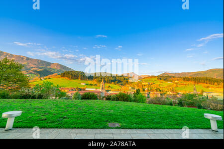 Green grass field on hill. Landscape of village in valley. Pine forest on the mountain with blue sky and white clouds on sunny day in Europe. Empty Stock Photo