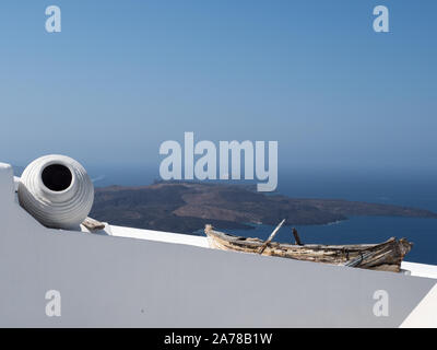 a view of vase pot salvaged, repurposed rowing boat on top a white wall distant mountains sea blue sky horizon Fira Santorini Stock Photo