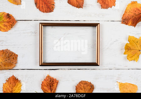 Autumn composition background. Square shape from rusty leaves with blank photo frame on white timber .Top view, copy space, flat lay . Stock Photo