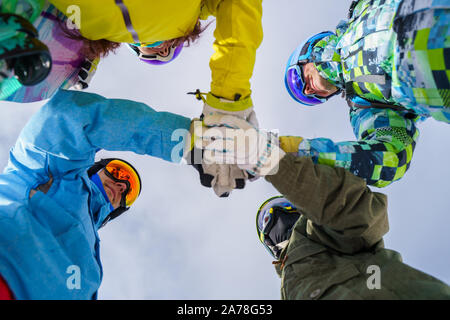 Image below of four snowboarders wearing helmet and mask doing handshake on blue sky background Stock Photo