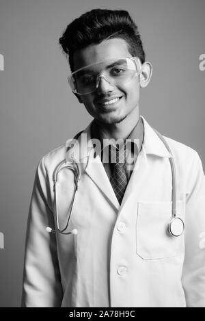 Young Indian man doctor wearing protective glasses against gray background Stock Photo