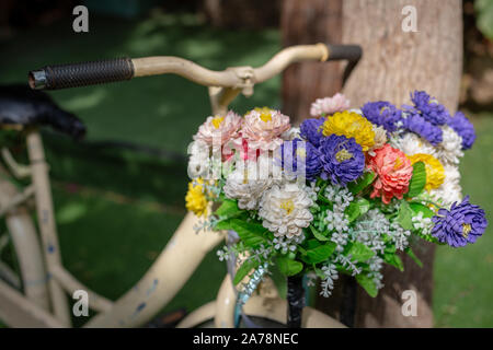 An old bicycle on a green background is leaning against a tree with colorful flowers on it. Stock Photo