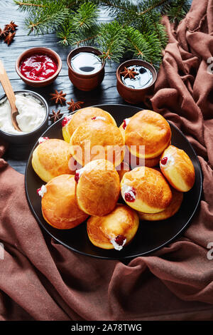 close-up of Berliner krapfen, German Donuts with Raspberry Jam and cream fillings on a plate. fir limbs and cups of coffee on a black wooden table, ve Stock Photo