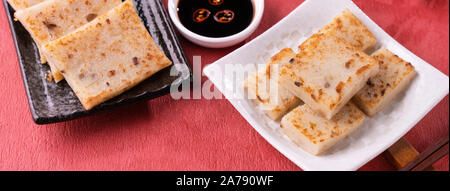 Chinese lunar new year food concept, Delicious turnip radish cake, local cuisine in restaurant with soy sauce on red background, close up, copy space Stock Photo