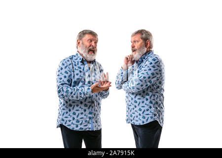 Senior man arguing with himself on white studio background. Concept of human emotions, expression, mental issues, internal conflict, split personality. Half-length portrait. Negative space. Angry. Stock Photo