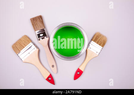 Brush with white handle on open can of green paint on grey pastel background. Main trend concept. Stock Photo