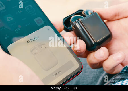 Bishkek, Kyrgyzstan - October 10, 2019: Man holds custom black airpods and connects them to iphone 11 Stock Photo