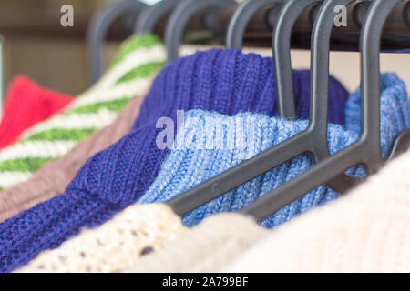warm knitted things, sweaters and dresses hang on hangers Stock Photo
