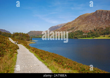 People tourists walkers walking along footpath walk beside Buttermere in autumn Lake District National Park Cumbria England UK United Kingdom Britain Stock Photo