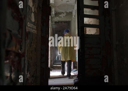 A man in helmet walking in radioactive ruins. A researcher with a flashlight in long corridor in destroyed and forgotten building. Nuclear symbol with Stock Photo