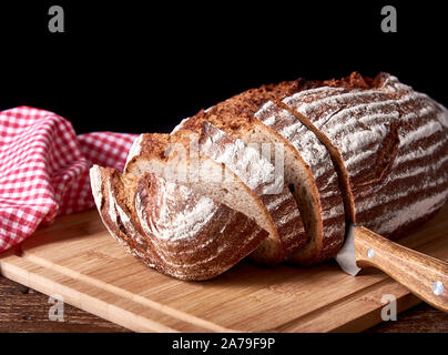 Still life on old wooden board table with sliced loaf of bread. Kitchen knife on black background and space for text. Stock Photo