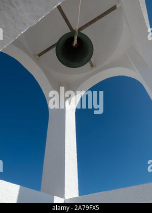 View from below of the church bell in a frame of the white bell tower and a beautiful blue sky Stock Photo